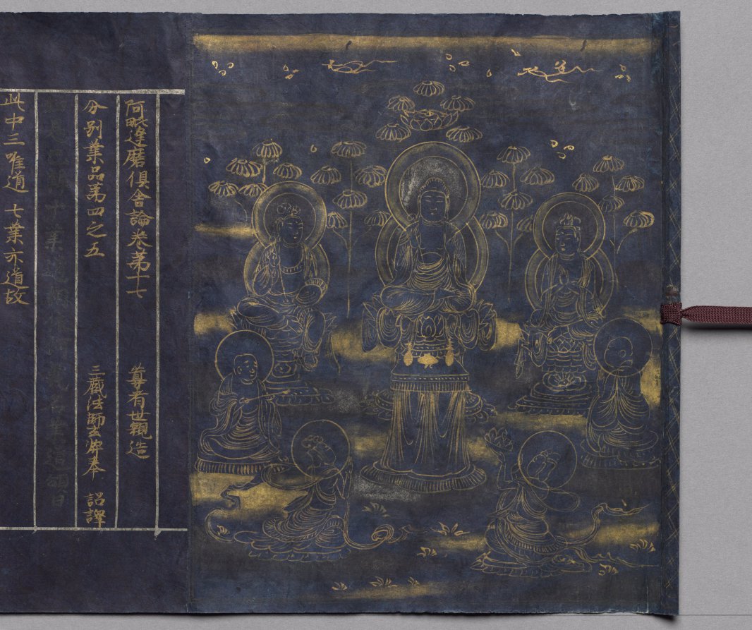 Gold-line frontispiece of a seated preaching Buddha with two bodhisattvas, monks and kneeling devotees, beside ruled title columns in gold and silver on indigo.