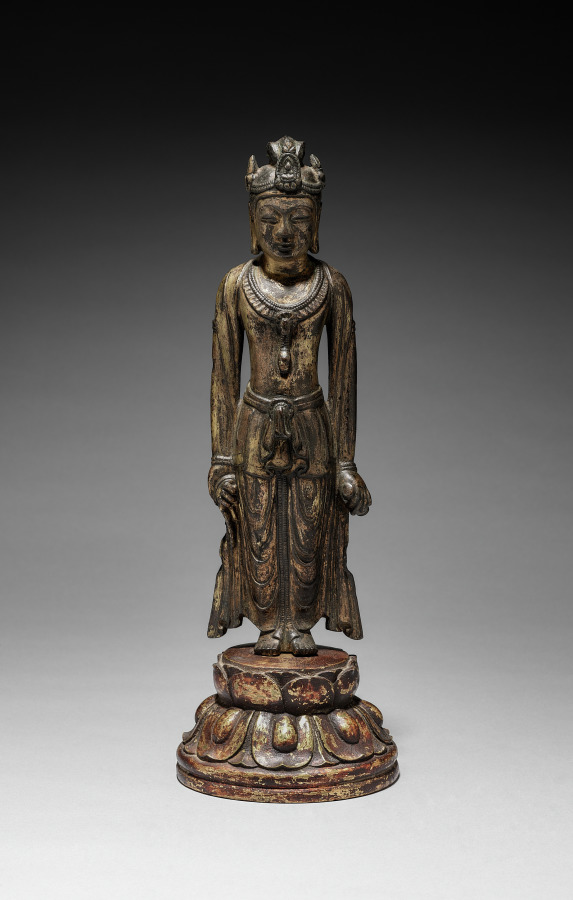 Asuka–Hakuhō gilt-bronze standing Kannon, mid-600s, 32 cm. Both arms hang at hip level; paired hip-flares; tiered round lotus pedestal.