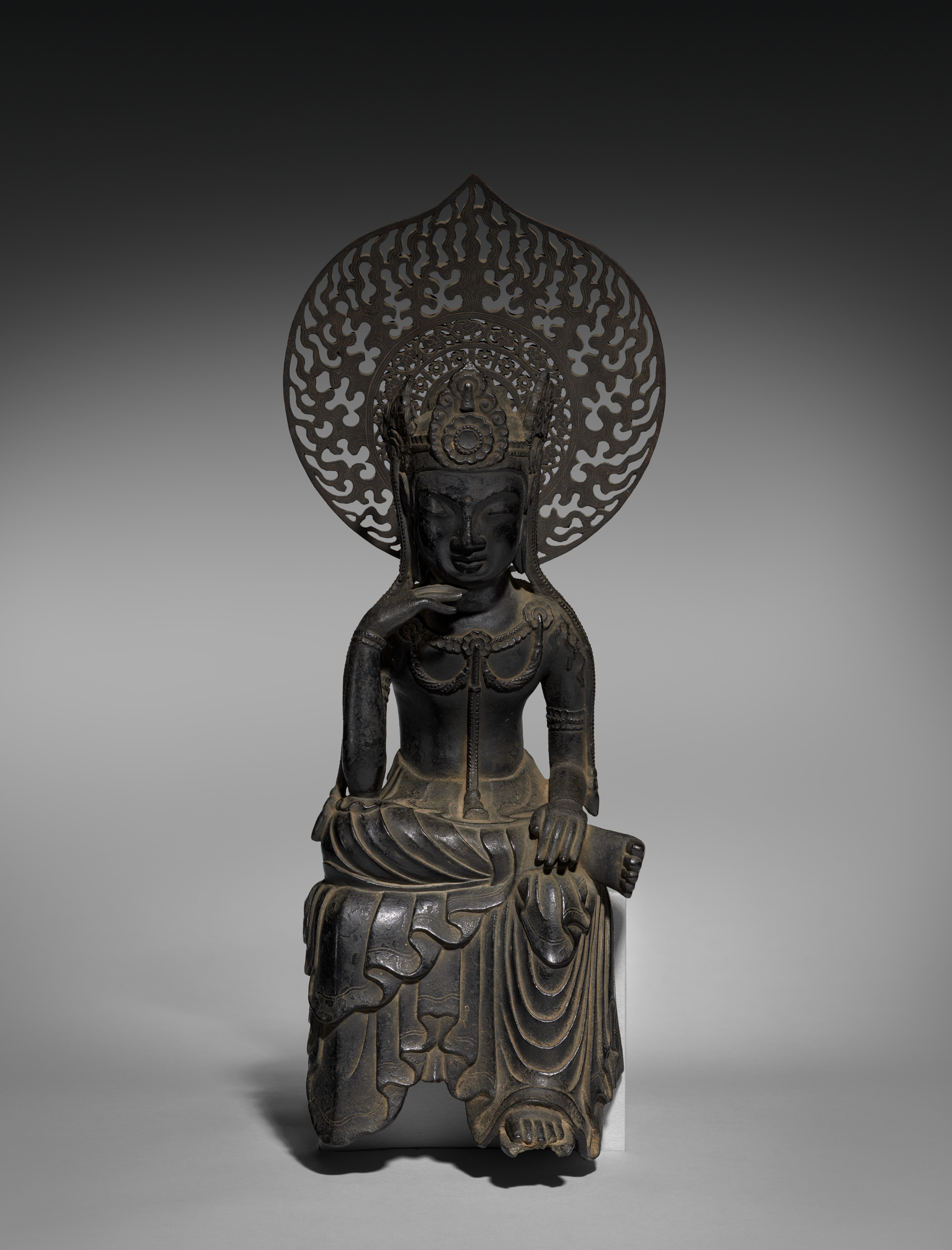 Asuka late-600s cast-bronze seated Miroku in hanka-shiyui half-lotus contemplation, 46 cm. Right hand at the cheek; openwork crown; tall flame-leaf mandorla behind.