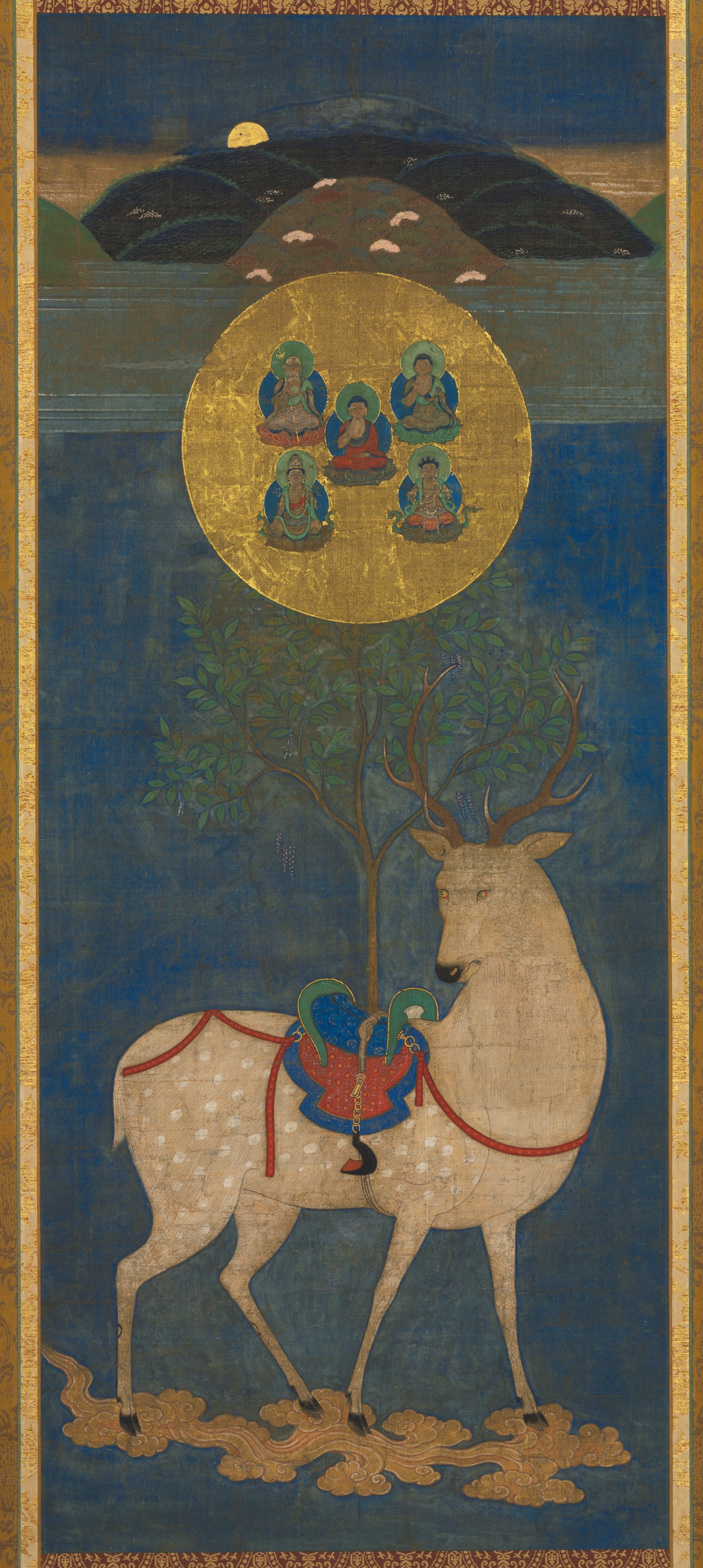 Nanbokuchō–Muromachi Kasuga deer mandala on indigo silk, mid-1300s–1400s. White deer with red saddle bears a sakaki branch; gold disc of five Buddhas above.