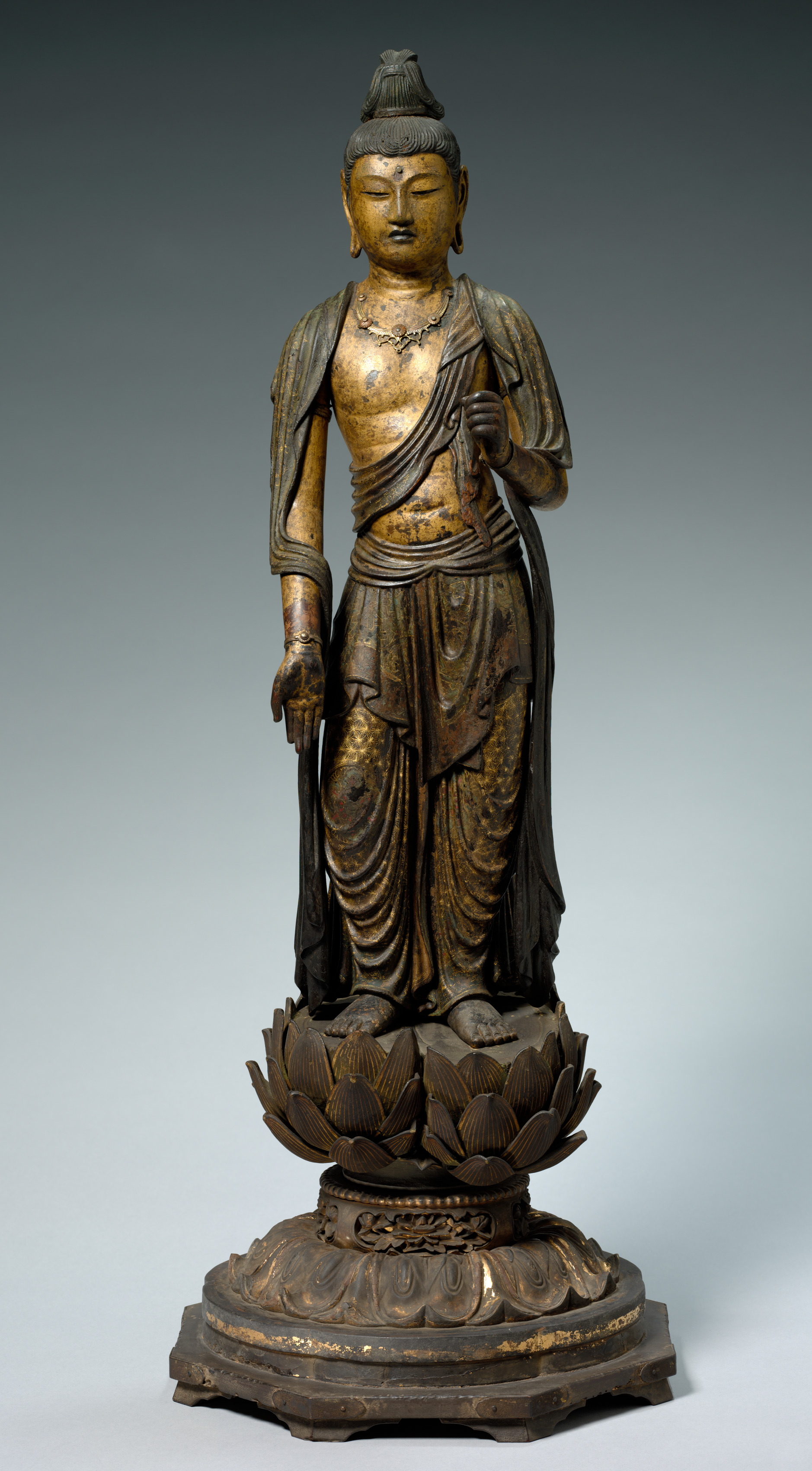 A standing wooden bodhisattva caught mid-step, one foot forward and the right knee bent, the torso swaying, in dark lacquered wood with worn gilding on a low base.
