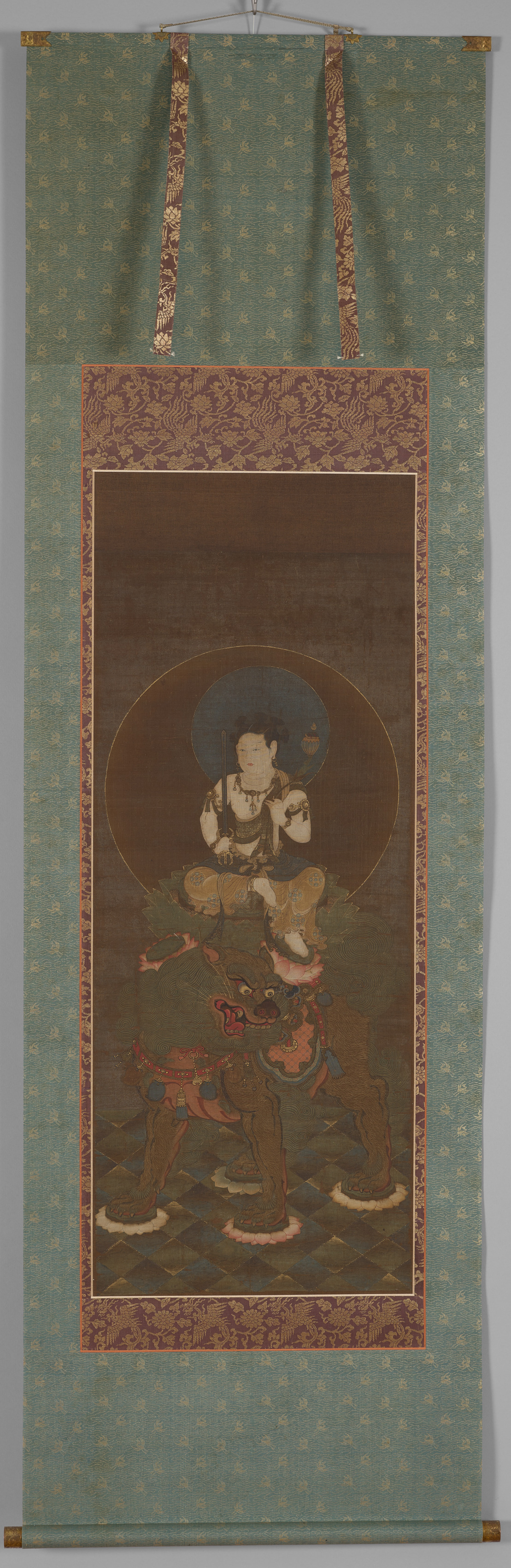 Hanging scroll of a youthful bodhisattva seated on a striding lion, a large circular halo behind, the lion stepping on four lotus pads, hair tied in knots, gold-painted mane.
