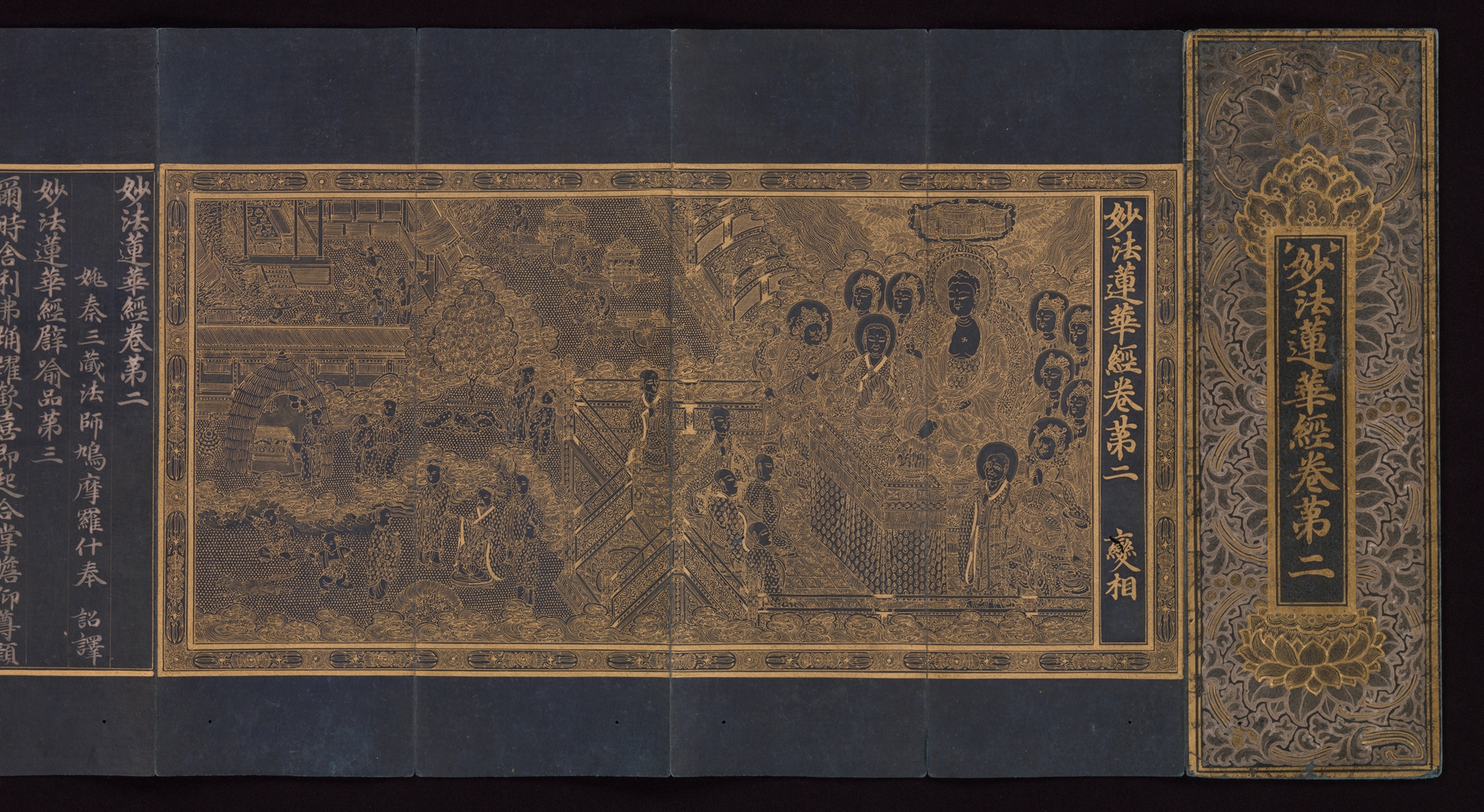 An opened Goryeo accordion-fold sutra book on a dark indigo ground. A gold-line frontispiece painting fills the centre: the Buddha enthroned at the right under a jeweled canopy