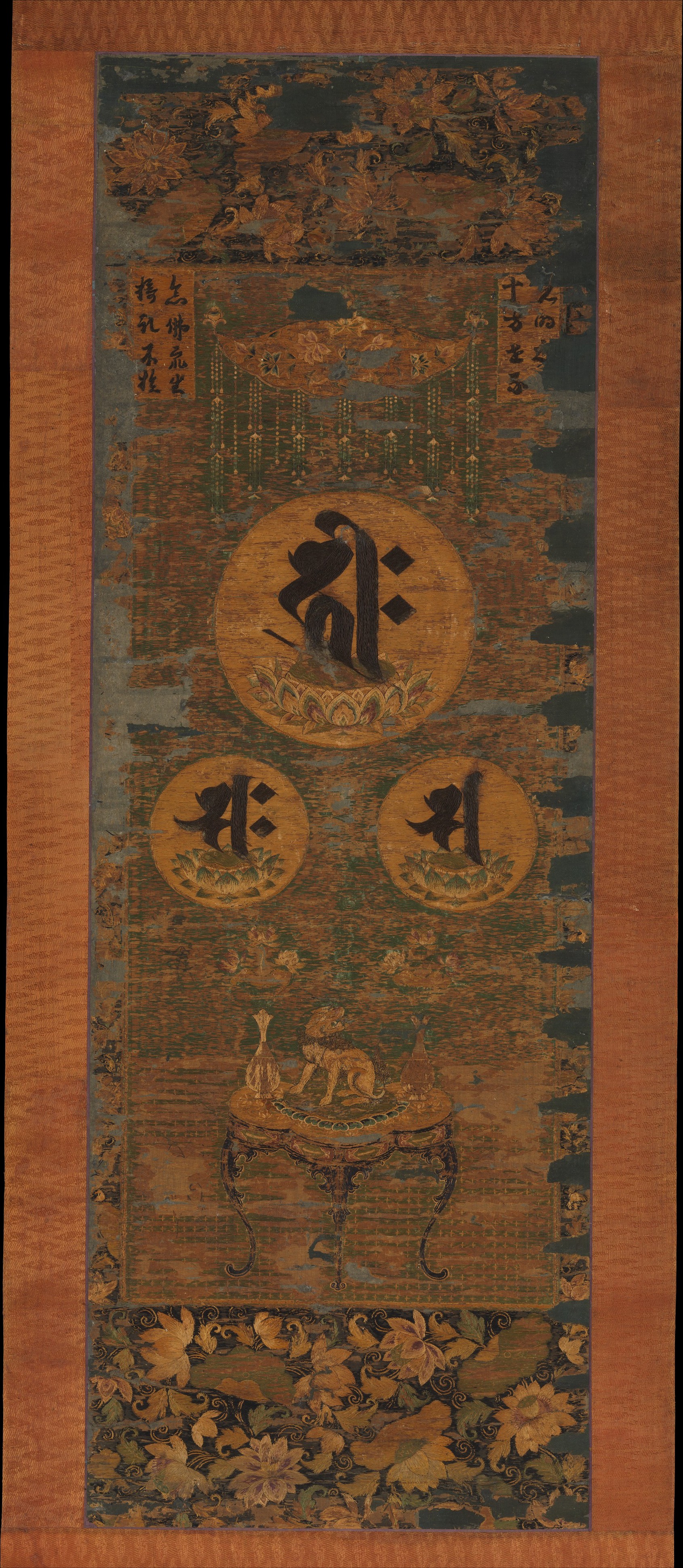 Kamakura 13th-c. embroidered hanging scroll in silk, gold-wrapped thread, and human hair, 114 × 39 cm. Three Sanskrit seed-syllables — Amida, Kannon, Seishi — above an altar.