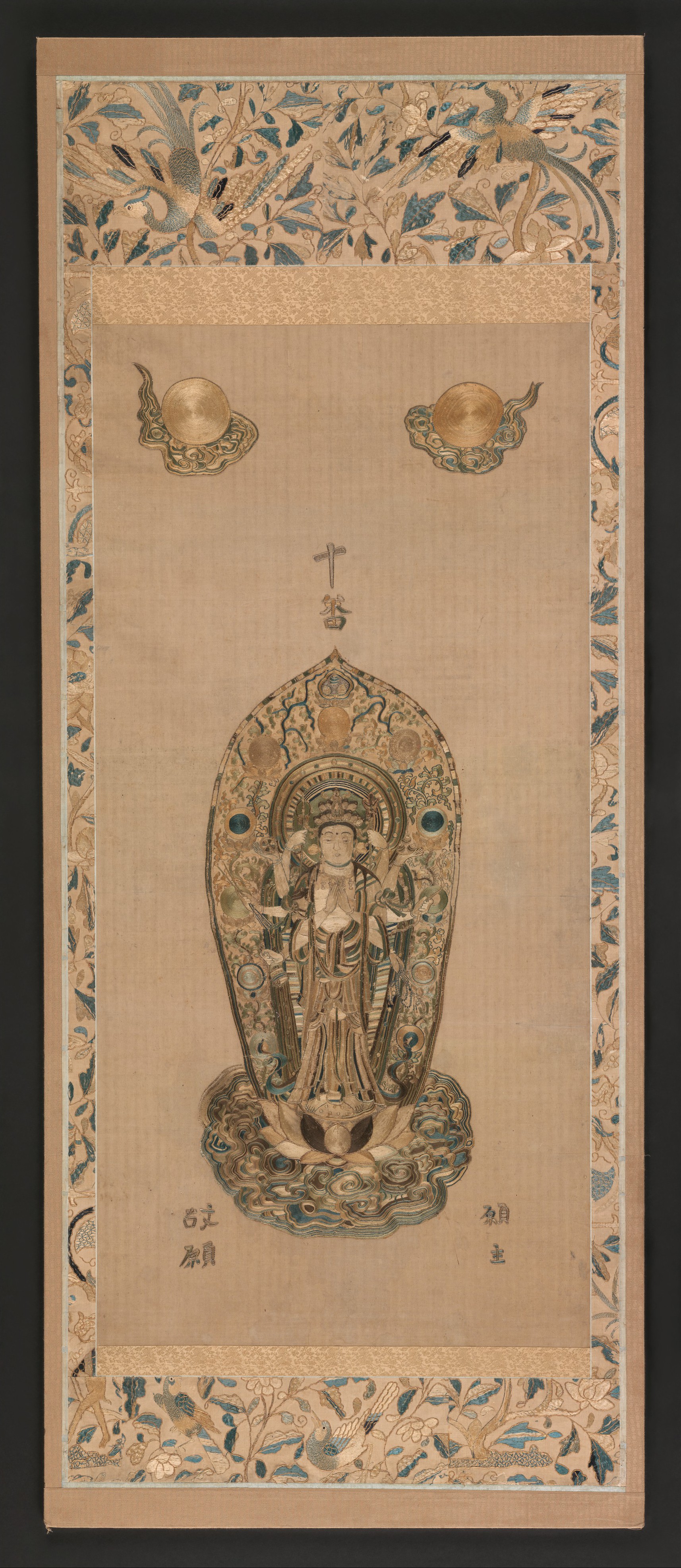 Late-Muromachi embroidered hanging scroll in silk on cotton, 15th–16th c., 195 × 79 cm. Senju Kannon, eleven heads, central hands in gasshō, the rest fanning out with attributes.