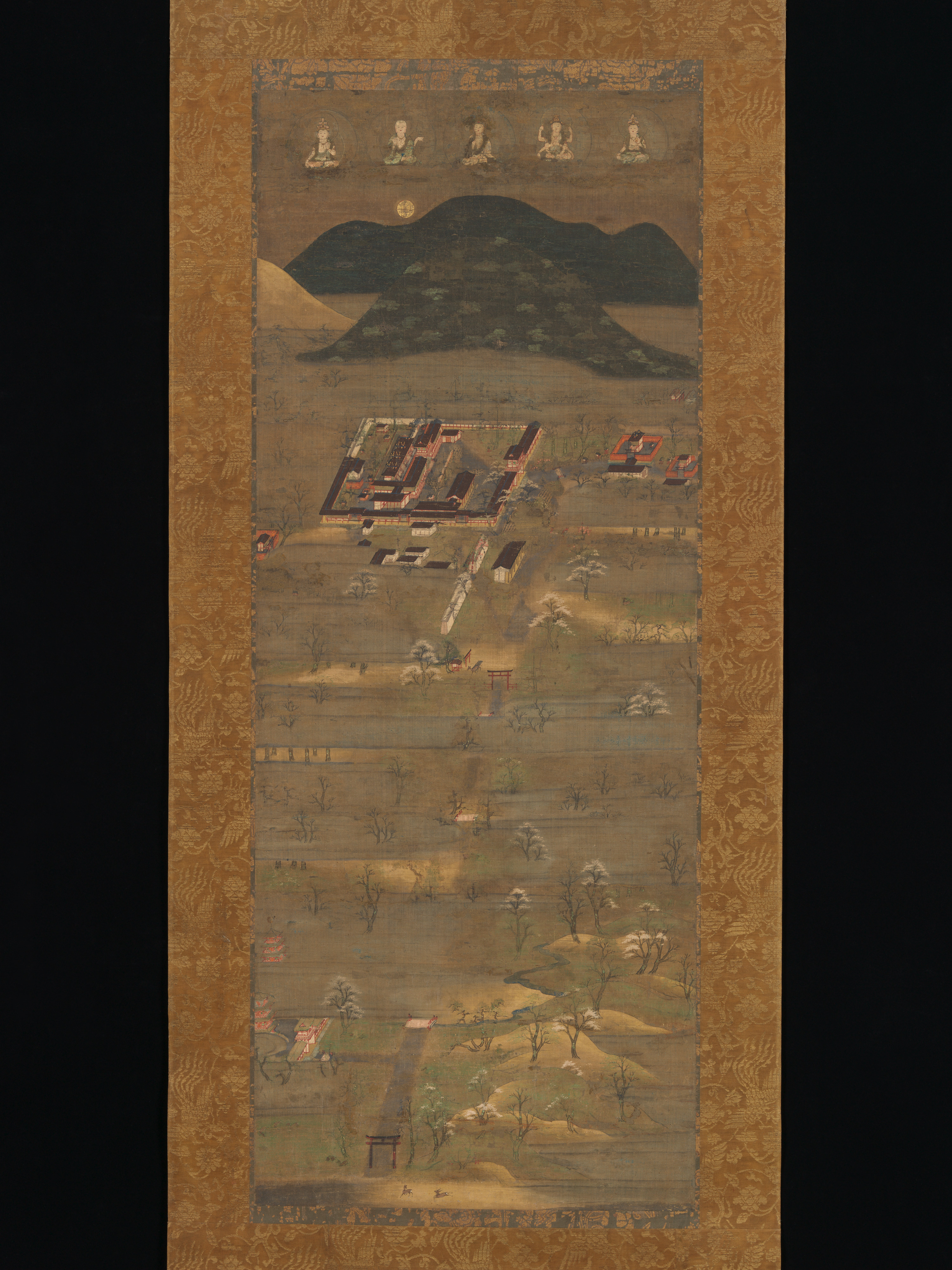 Kamakura early-14th-c. Kasuga shrine mandala, ink colour and gold on silk, 100 × 40 cm. Same vertical-climb composition as the Oba scroll; taller mountain, warmer palette.