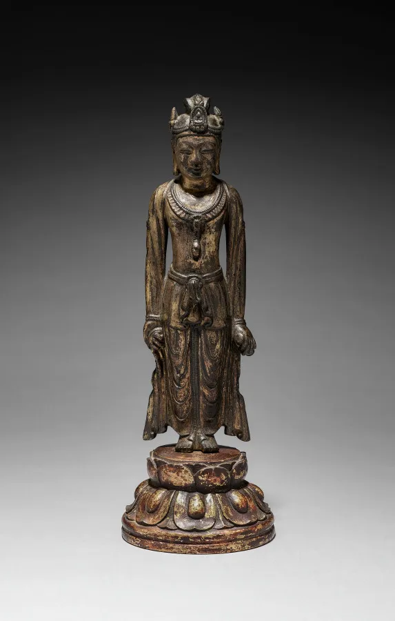 Asuka–Hakuhō gilt-bronze standing Kannon, mid-600s, 32 cm. Both arms hang at hip level; paired hip-flares; tiered round lotus pedestal.