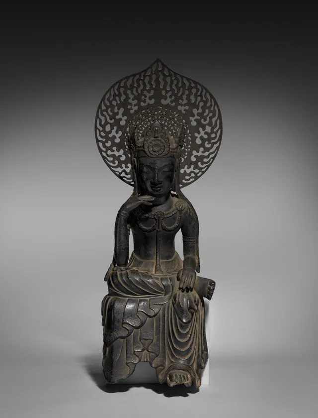 Asuka late-600s cast-bronze seated Miroku in hanka-shiyui half-lotus contemplation, 46 cm. Right hand at the cheek; openwork crown; tall flame-leaf mandorla behind.