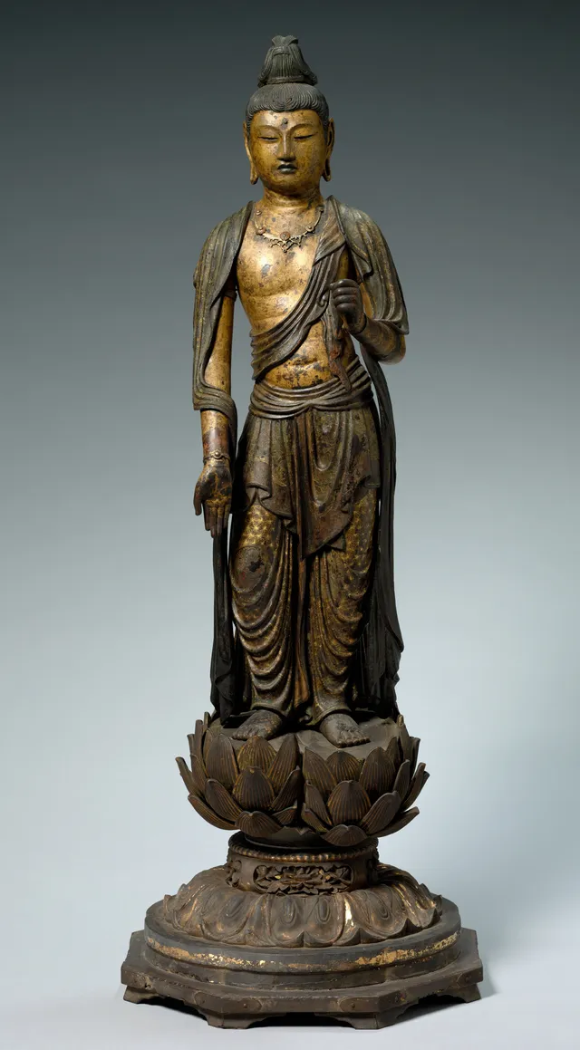 A standing wooden bodhisattva caught mid-step, one foot forward and the right knee bent, the torso swaying, in dark lacquered wood with worn gilding on a low base.