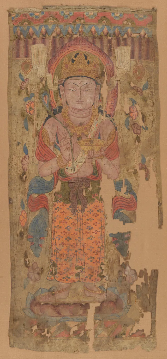 A tall narrow painted-silk banner: a standing deity on a lotus, facing front, a peacock feather in the right hand and a bowl in the left; the silk split down one side.