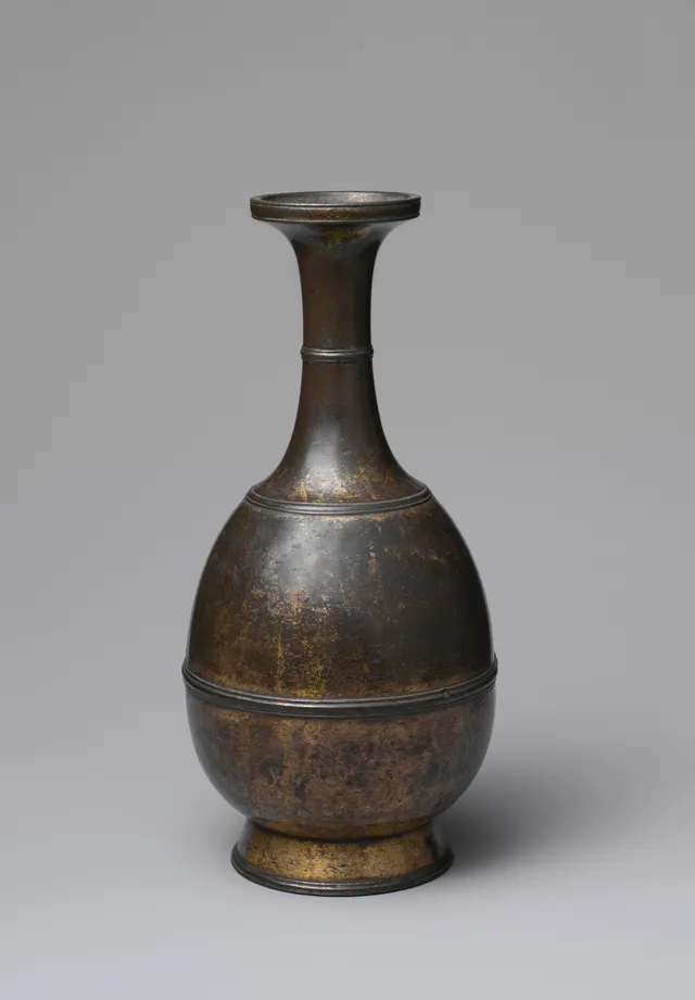 A small bottle-shaped bronze altar vessel with a flaring dish mouth, ringed neck and splayed foot; gilding survives in the hollows and is worn to dark bronze on the shoulder.