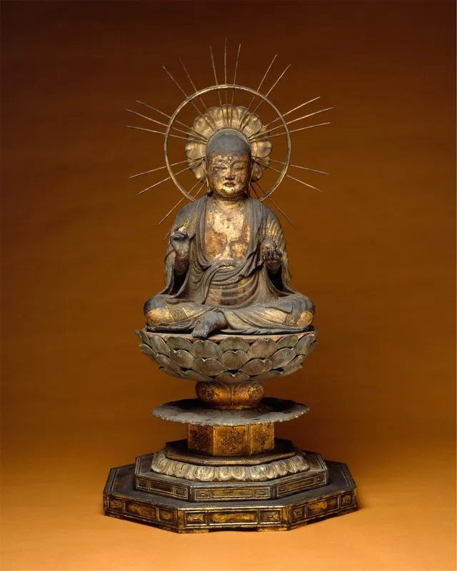 A small standing wooden Jizō, a shaven-headed monk in a robe over both shoulders, on a tall lotus pedestal with a flame-edged halo, the lacquer darkened.