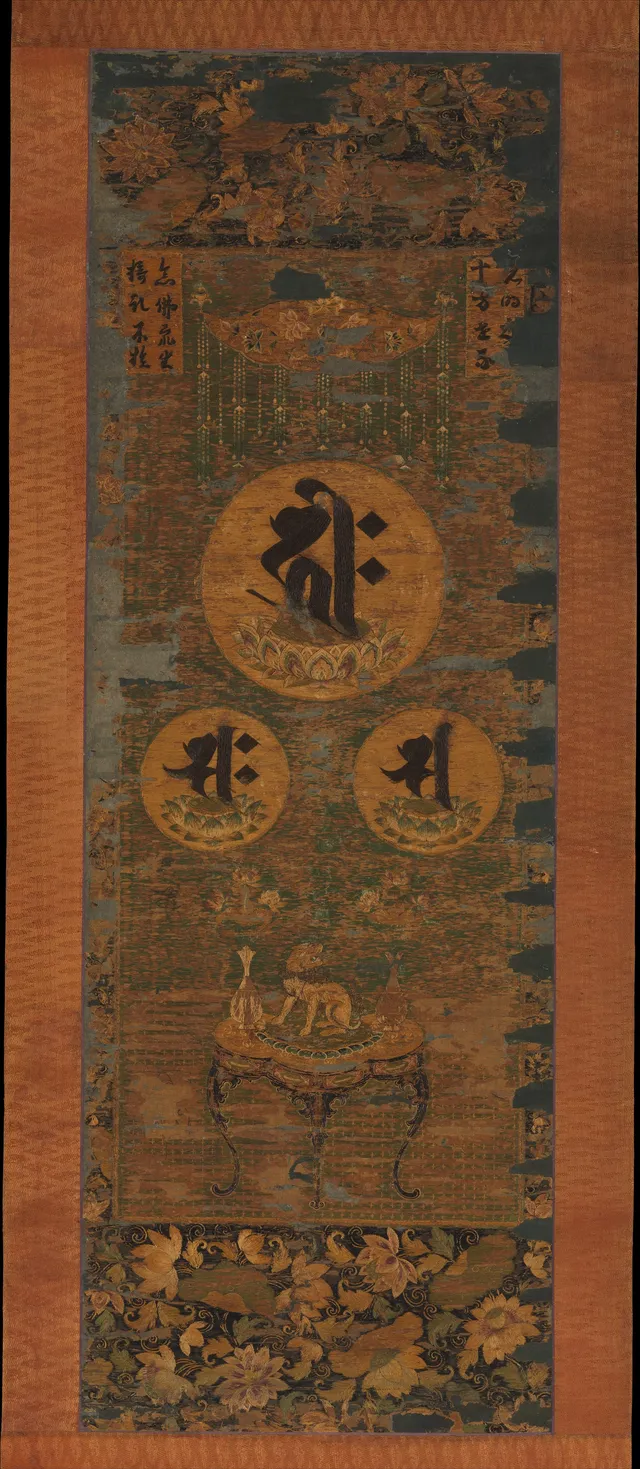 Kamakura 13th-c. embroidered hanging scroll in silk, gold-wrapped thread, and human hair, 114 × 39 cm. Three Sanskrit seed-syllables (Amida, Kannon, Seishi) above an altar.