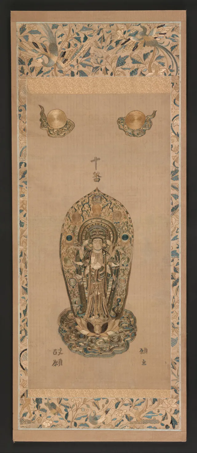 Late-Muromachi embroidered hanging scroll in silk on cotton, 15th–16th c., 195 × 79 cm. Senju Kannon, eleven heads, central hands in gasshō, the rest fanning out with attributes.