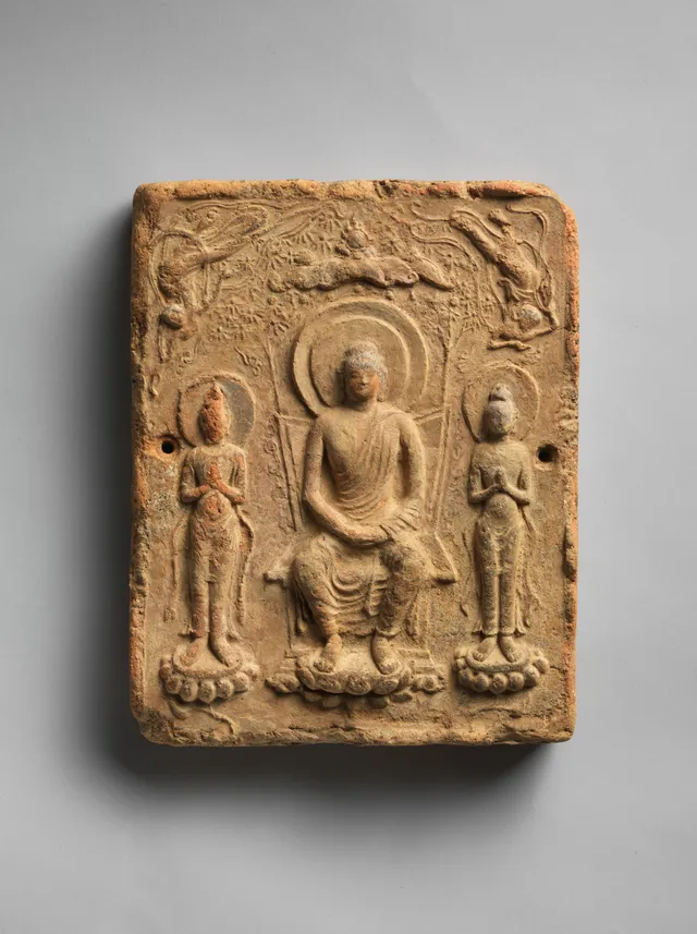 Asuka late-7th-c. earthenware relief tile, 24.5 × 19.7 × 3.8 cm. Press-moulded sanzon senbutsu: central seated Buddha beneath a canopy, two standing bodhisattvas.